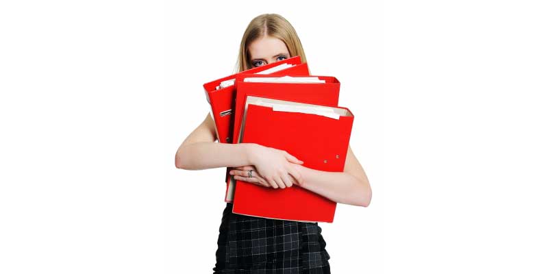 An overworked businesswoman holding many binders
